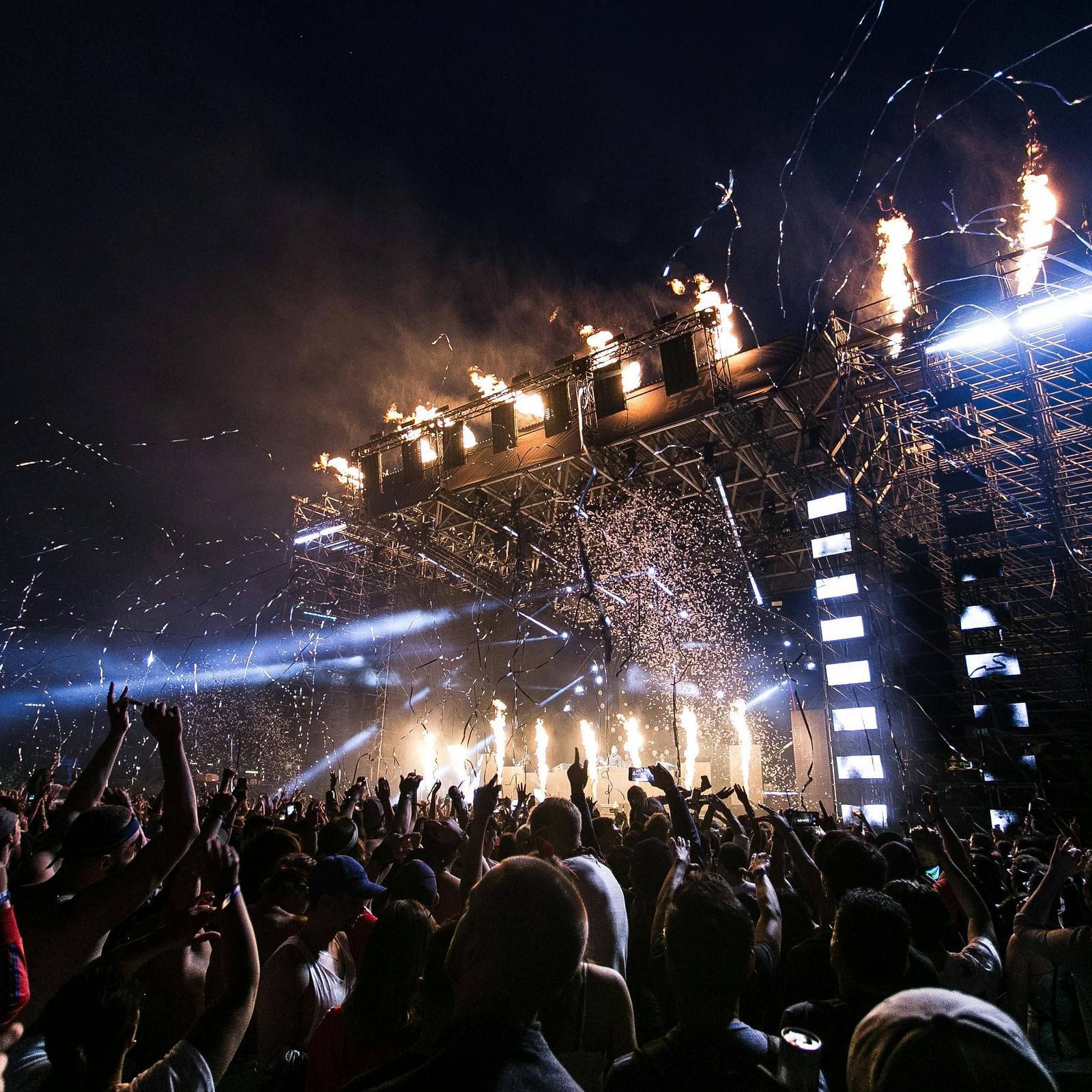 A vibrant crowd enjoying a music festival, illuminated by fireworks in the night sky.
